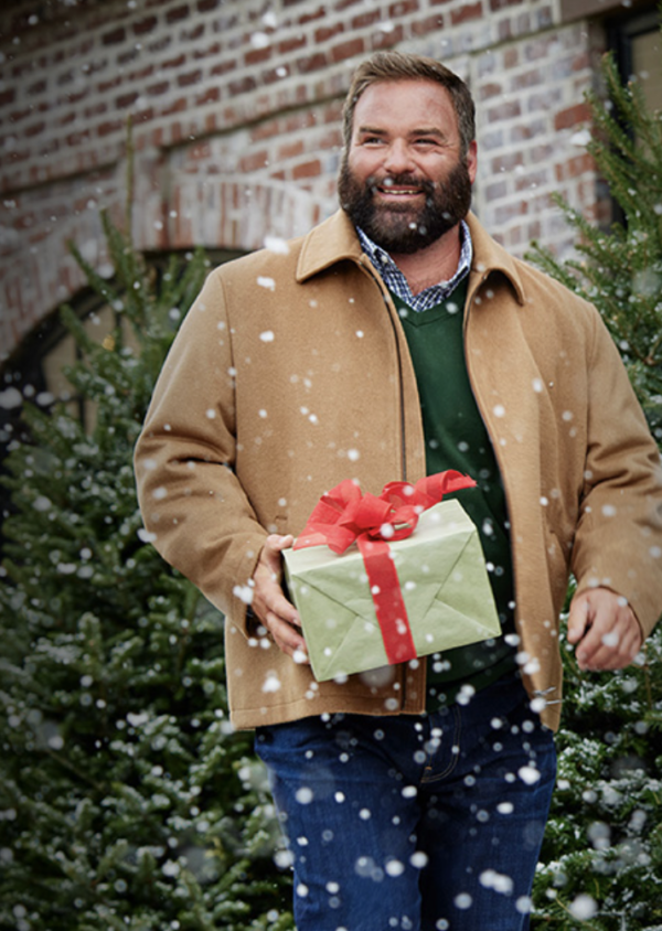 Happy man in tan coat carrying a wrapped gift